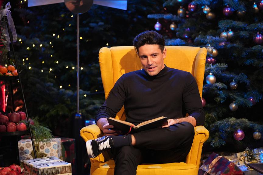 Alexander Eder liest auf einem gelben Stuhl eine Weihnachtsgeschichte vor. 