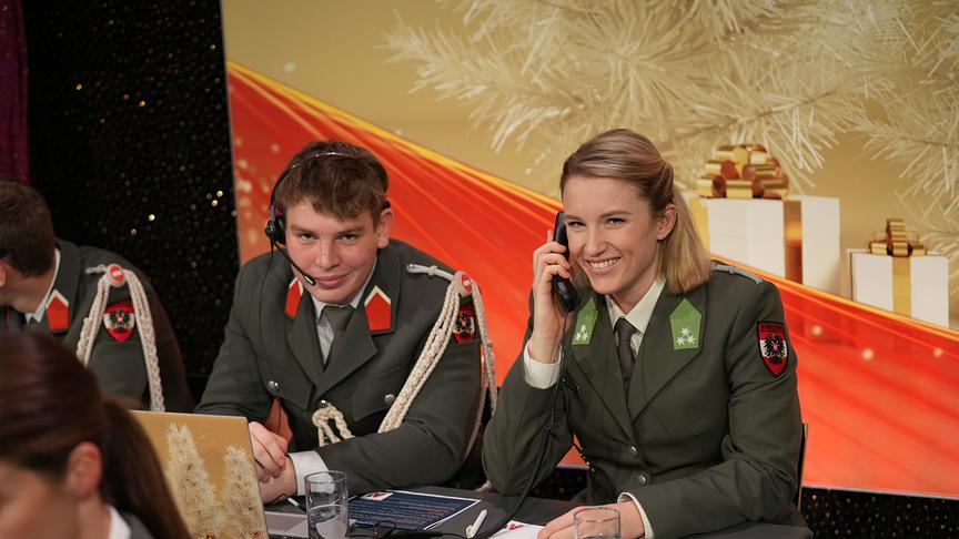 Ein Heeressportler und eine Sportlerin telefonieren und lächeln in die Kamera 