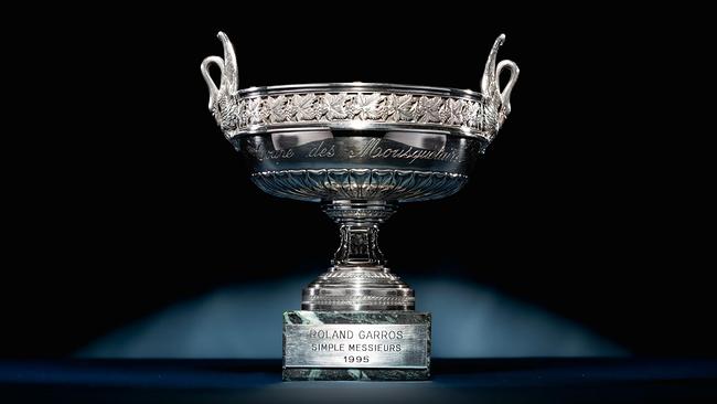 Eine silberne Trophäe vor dunklem Hintergrund. Sie trägt die Aufschrift "Coupe des Mousquetaires", ist mit detaillierten Verzierungen versehen und hat zwei elegante Griffe in Flügelform. Auf dem Sockel ist "Roland Garros Simple Messieurs 1995" eingraviert.