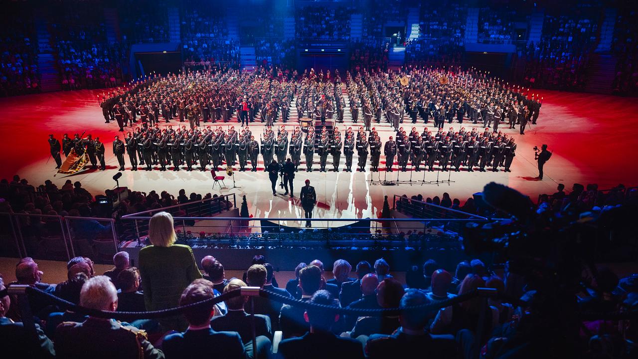 © Österreichisches Bundesheer Vom Publikum aus sind die Militärmusiken und die Ehrenkompanie mit hunderten Personen zu sehen, die für den Großen Österreichischen Zapfenstreich in Formation stehen. Bundesministerin Tanner ist von hinten zu sehen, sie steht als einzige inmitten des sitzenden Publikums. Der Kommandant der Garde steht ihr zugewandt auf der Saalfläche.