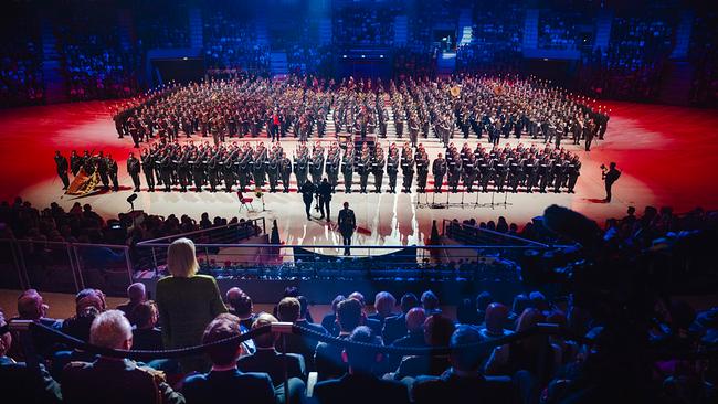 Vom Publikum aus sind die Militärmusiken und die Ehrenkompanie mit hunderten Personen zu sehen, die für den Großen Österreichischen Zapfenstreich in Formation stehen. Bundesministerin Tanner ist von hinten zu sehen, sie steht als einzige inmitten des sitzenden Publikums. Der Kommandant der Garde steht ihr zugewandt auf der Saalfläche.