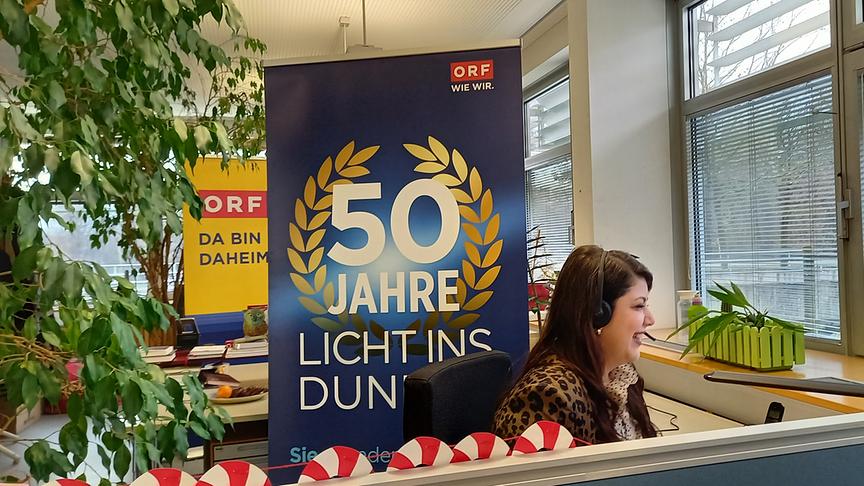 Eine Kollegin sitzt am Spendentelefon, im Hintergrund zwei Rollups mit dem Logo von 50 Jahre LICHT INS DUNKEL und ORF Radio NÖ.