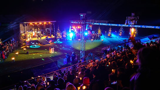 Das Publikum blickt von der Tribüne auf die Bühne auf dem Fußballfeld. Das Stadion ist weihnachtlich geschmückt.
